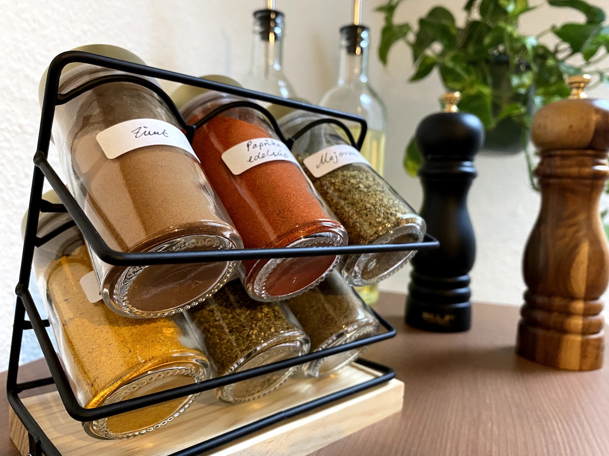 A spice rack houses six glass jars of various spices, including paprika and thyme, arranged in a metal holder. Behind are two elegant oil dispensers and a pair of wooden salt and pepper shakers, complementing the kitchen's functional decor.