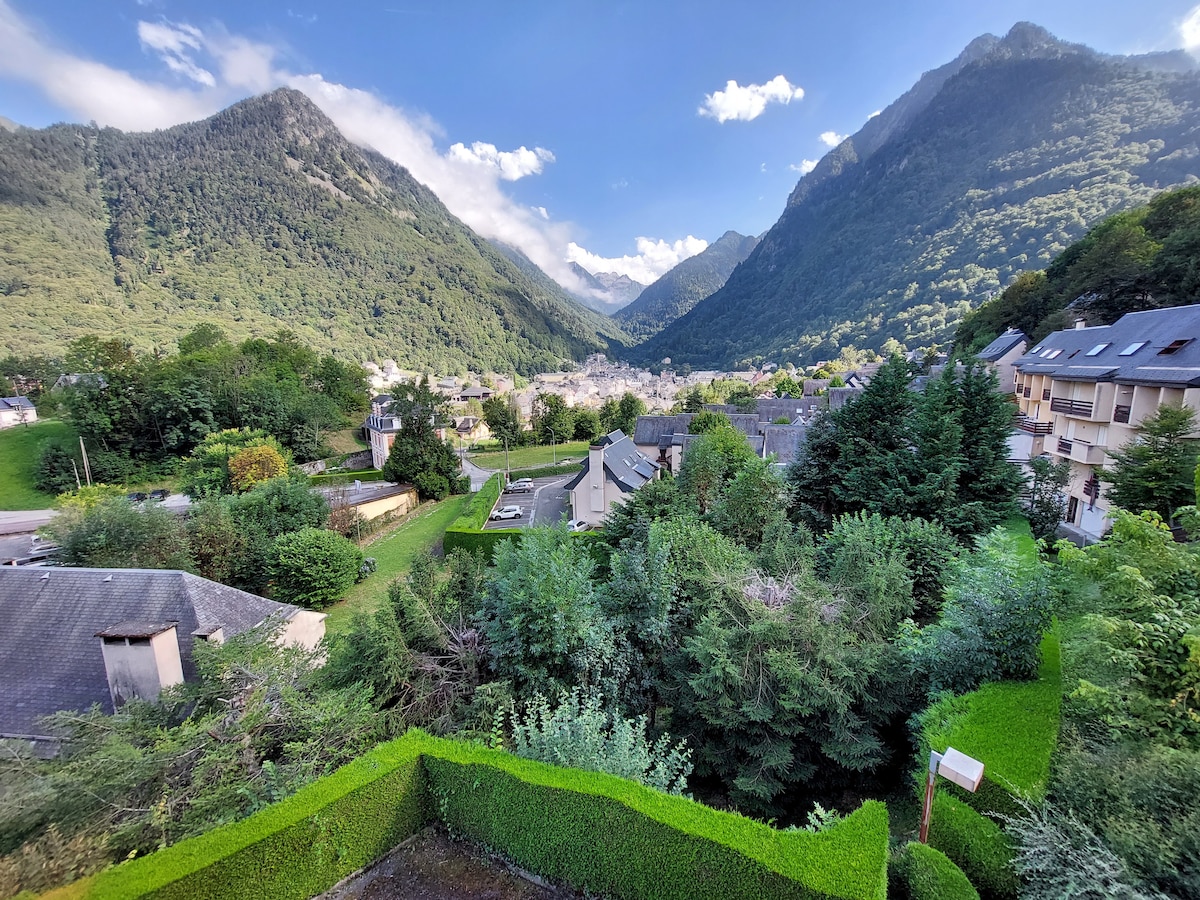 A sweeping view captures the surrounding mountains and lush greenery, creating a serene backdrop. The village of Cauterets can be seen nestled within the valley, framed by hills on either side. The landscape appears tranquil and inviting.