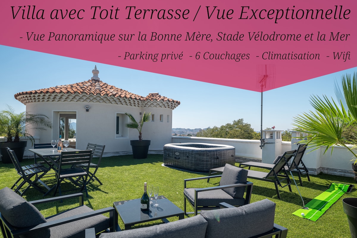 The rooftop terrace features a spacious area with a synthetic lawn, a Jacuzzi accommodating six, and a dining table with chairs. Breathtaking views of Marseille, including the sea and Bonne Mère, are visible. Sun loungers offer relaxation in this well-equipped outdoor space.