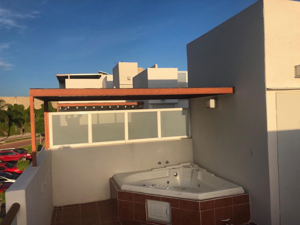 A private jacuzzi is situated on a spacious balcony, surrounded by a low railing and partial walls for privacy. The area is enhanced by a wooden overhang, and a clear sky is visible beyond the surrounding buildings.