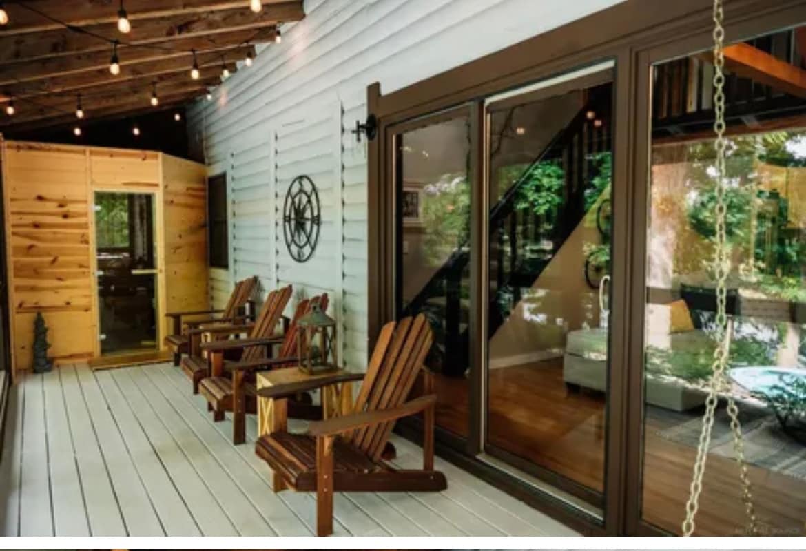 A spacious screened porch features multiple wooden adirondack chairs, inviting relaxation. Glass doors offer a view into the interior, where natural light highlights the wooden accents. Decorative elements, such as a wall hanging and outdoor lighting, create an inviting outdoor setting.