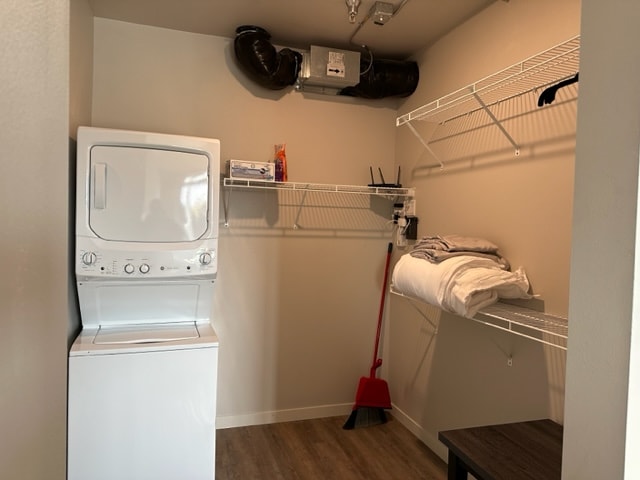 A laundry area is provided, featuring a stacked washer and dryer unit. Wire shelving is installed along one wall, with towels and a broom visible. The space is simply decorated with a neutral color palette and has a clean, functional appearance.