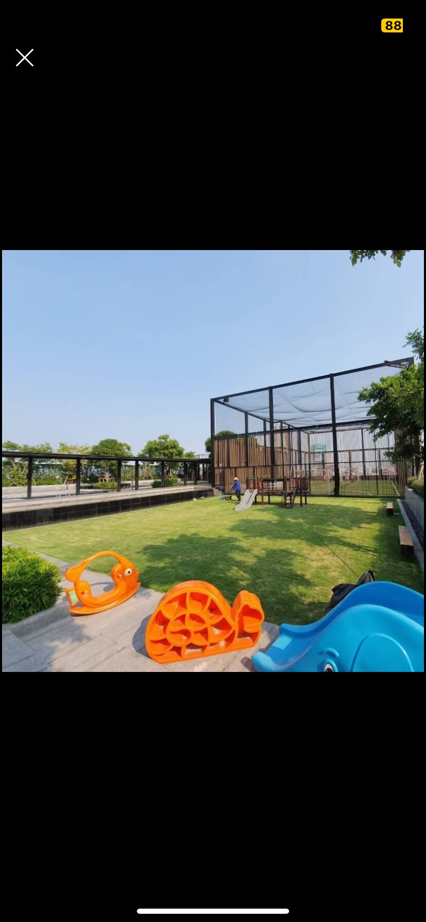 A well-maintained outdoor play area features a grassy expanse surrounded by a secure enclosure. Colorful play structures, including an orange slide and climbing features, are positioned on the lawn, offering a safe space for children to enjoy outdoor activities.