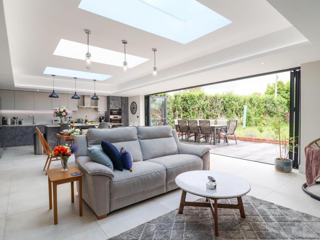 A spacious, open-plan living area features a comfortable sofa and a coffee table, with natural light pouring in through skylights. Large glass doors lead to an outdoor dining area, creating a seamless connection between indoor and outdoor spaces.