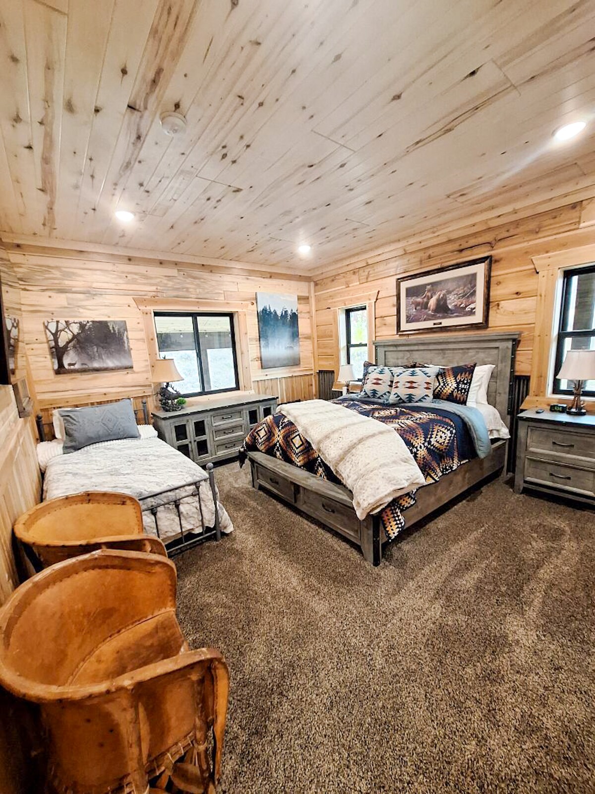 Een ruime slaapkamer met een kingsize bed met zacht beddengoed, sierkussens en een gezellig dekentje, plus een eenpersoonsbed dat ideaal is voor een extra gast of kind. De kamer is voorzien van een tv en nachtkastjes.