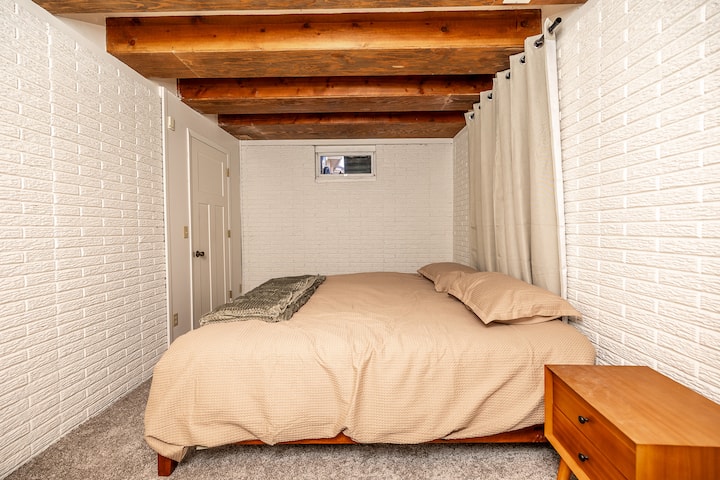 Ქვედა დონის საძინებელი აყვავებული თეთრეულით, სხივის ჭერითა და არაგაბარიტული კარადაში ჩაფლული ვანა-ტუალეტით დამატებითი კომფორტისთვის.
