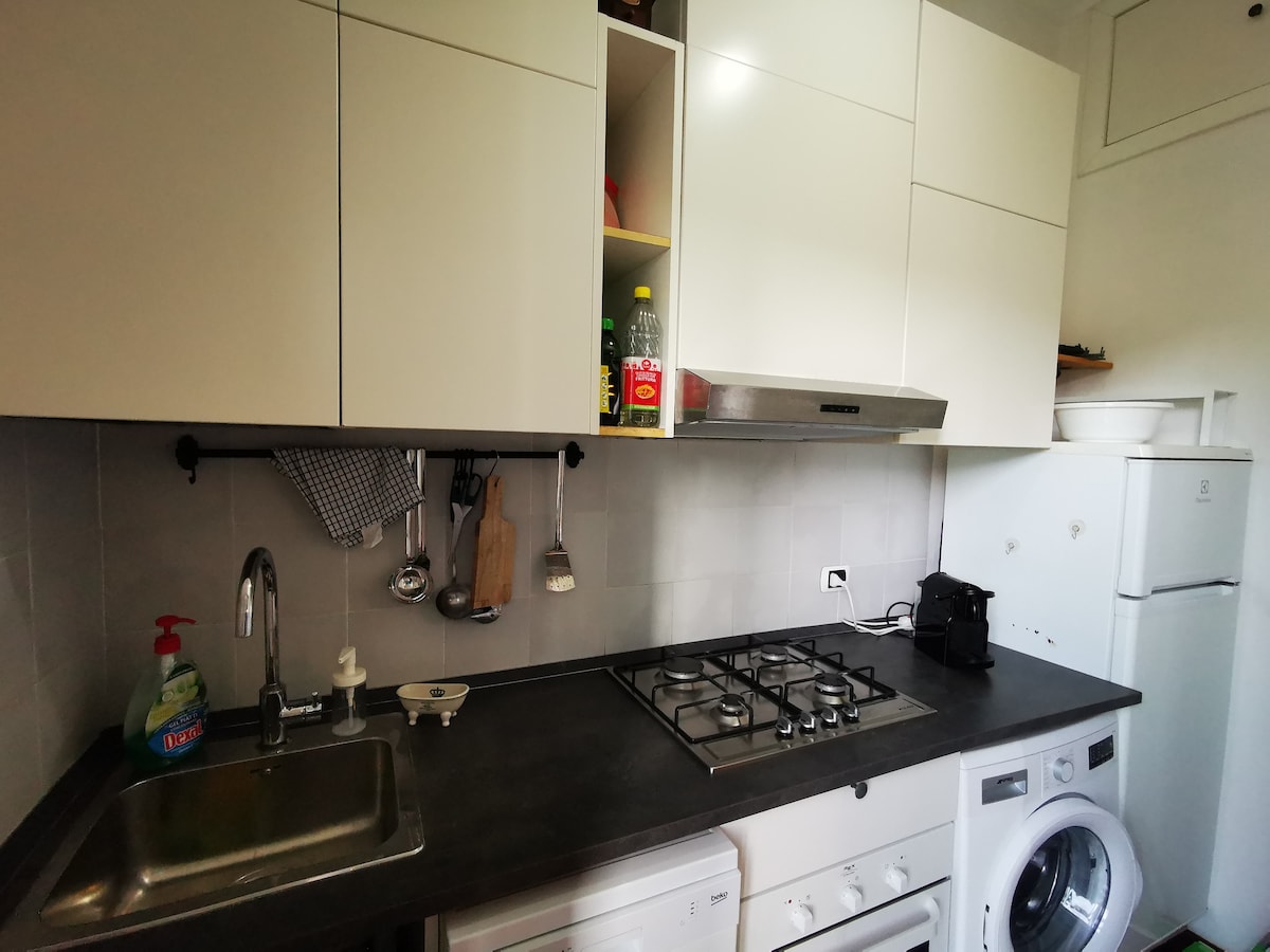The kitchen features modern cabinetry and a sleek countertop. A stainless steel sink is located beside a gas stovetop with four burners. Essential appliances are present, including a washing machine and refrigerator, creating a functional space for meal preparation and laundry.