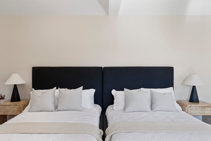 Ფართო საძინებელი ლუქს-კლასის 7-საძინებლიან საცხოვრებელში მომხიბვლელ ჩესტერში, რომელშიც არის ორი ერთადგილიანი საწოლი, დიდი ფანჯრები ბუნებრივი განათებით და ორი საწოლისპირა მაგიდა ელეგანტური ლამპებით მყუდრო, მშვიდი ატმოსფეროსთვის.