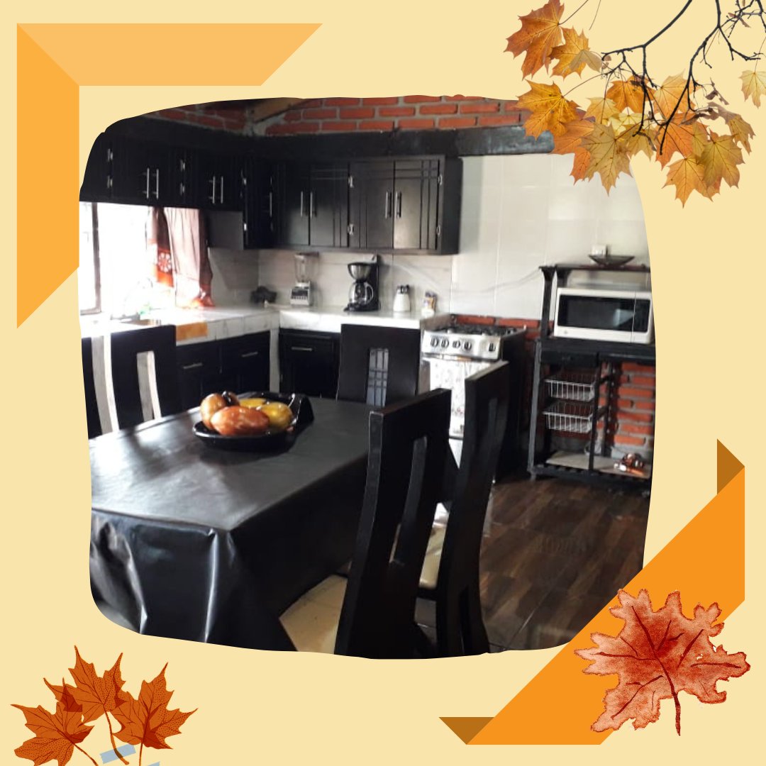 A kitchen area features dark cabinetry paired with a light countertop. A dining table with black tablecloth and chairs is positioned in the center, complemented by a bowl of fruit. Kitchen appliances include a stove, microwave, and coffee maker, with a brick wall adding texture.
