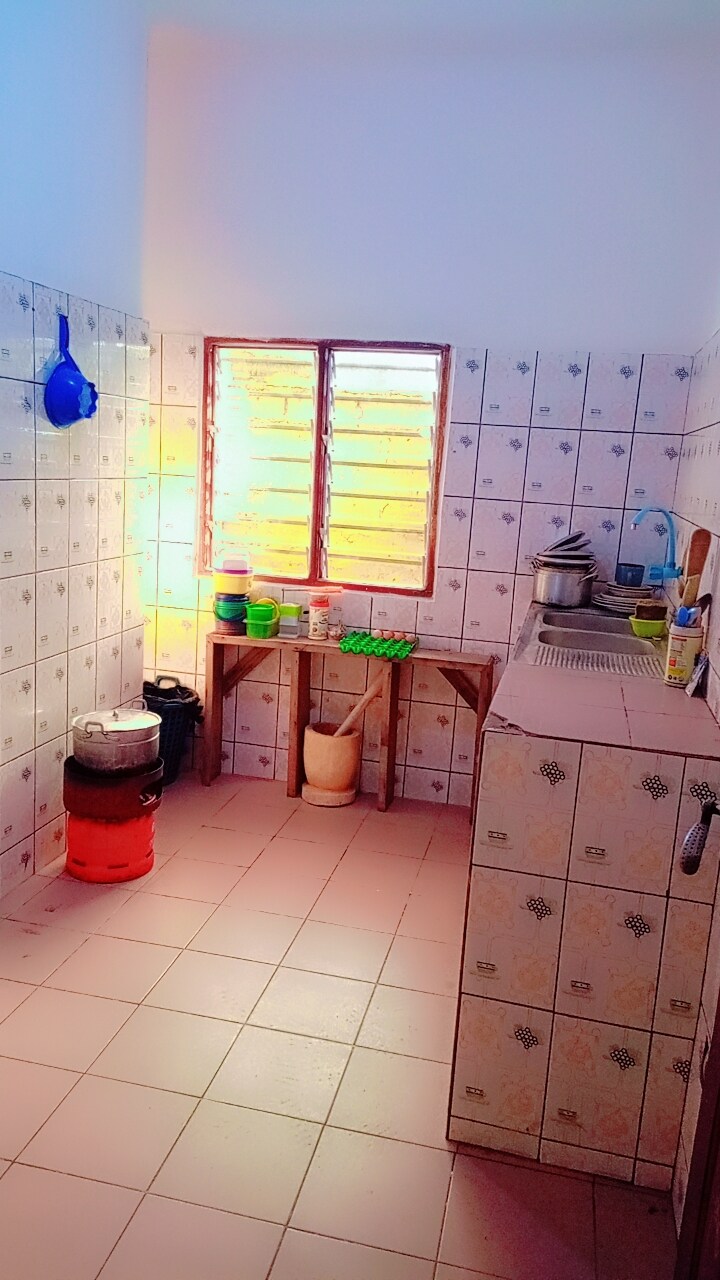 The kitchen features tiled walls and a window allowing natural light to enter. A wooden counter is equipped with utensils and cooking supplies, while various containers are organized on the shelves. The floor is tiled, contributing to the functional and tidy environment.