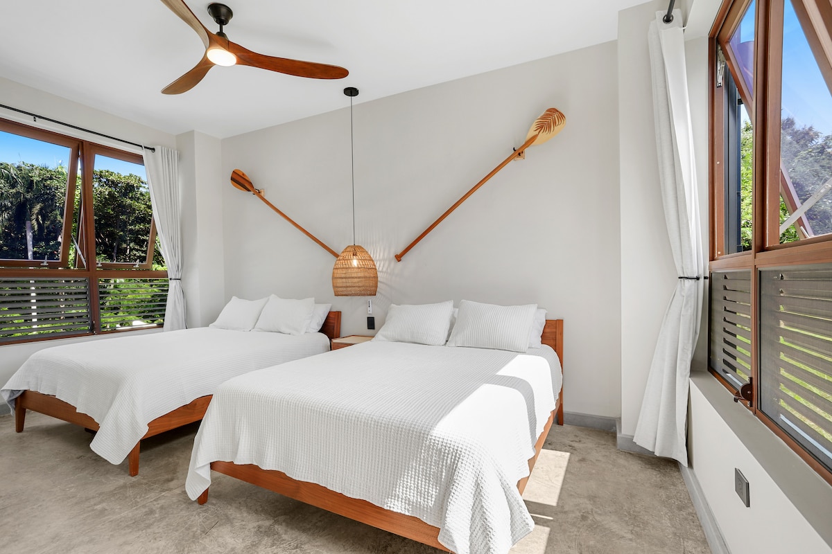 Dormitorio con dos camas tamaño queen.  Las ventanas ayudan a mantener la luz natural y la ventilación cruzada.  Cortinas oscuras para tener un buen sueño de noche de sueño.