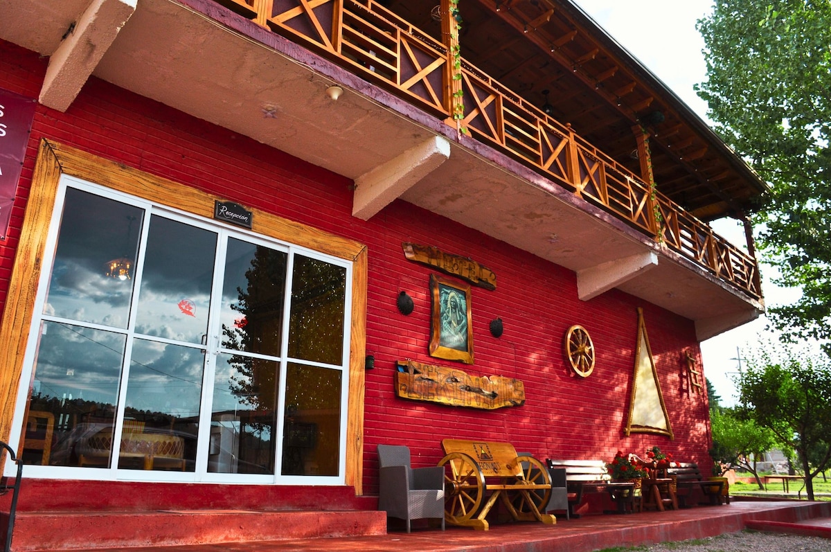 The exterior of the building features a vibrant red façade complemented by wooden accents. Large glass doors offer a welcoming entrance, while a balcony adorned with wooden railings provides an outdoor space. Decorative elements, including artworks and benches, enhance the inviting appearance.