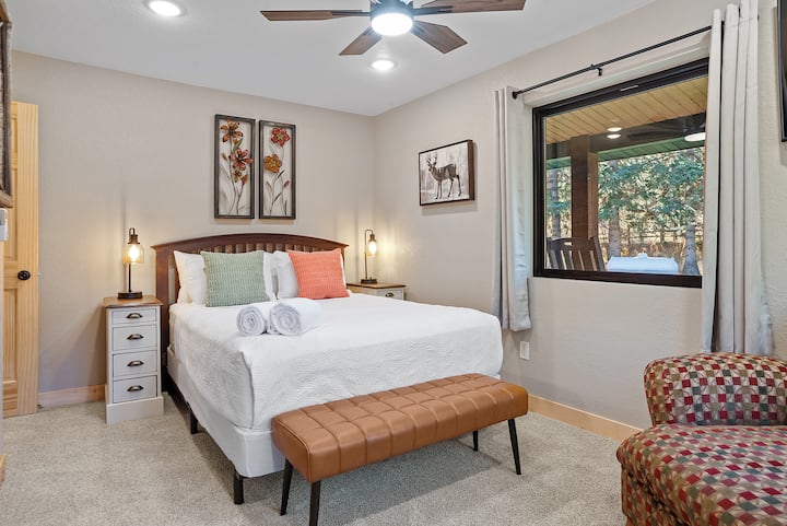 Enjoy a comfortable queen-sized bed with side tables and lamps, a ceiling fan for a cozy atmosphere, a TV for entertainment, and wide windows that flood the room with natural light.
