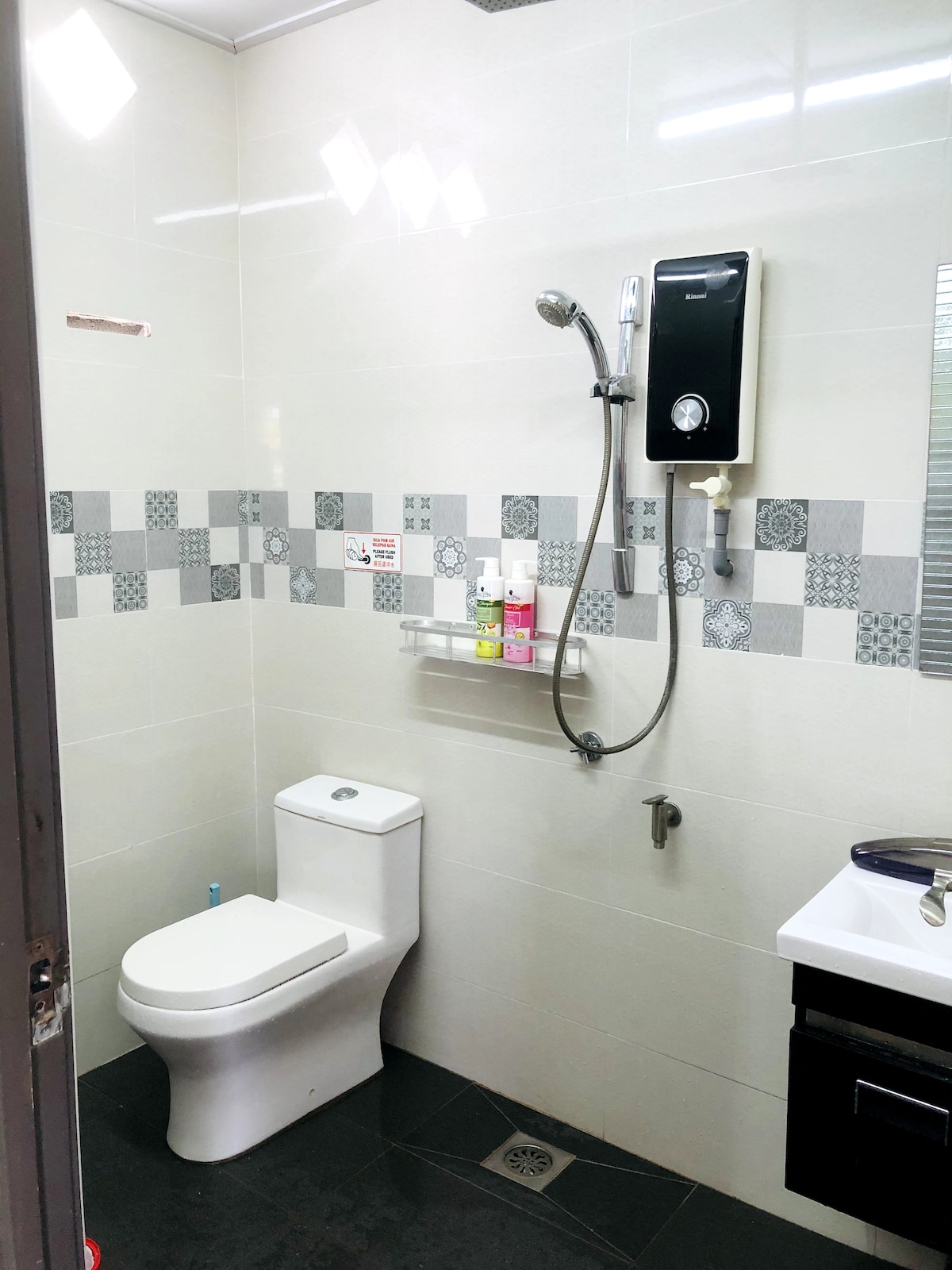 A clean bathroom is equipped with modern fixtures, including a toilet and a shower area. Shelving is provided for toiletries, with various bottles arranged neatly. A small sink is positioned next to the shower, complementing the overall design.