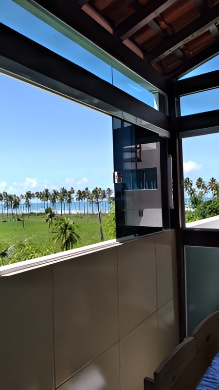 A large window offers a stunning view of palm trees and the ocean beyond. Natural light floods the space, illuminating the modern interior design. The window is partially open, inviting fresh air and the ocean breeze into the room.