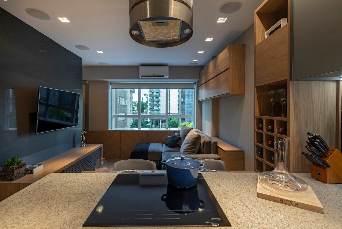 The kitchen area features a modern countertop with a cooktop and an assortment of kitchen tools. A large window allows natural light to fill the space, revealing views of the surroundings. The seating area includes a cozy couch, complemented by stylish cabinetry.