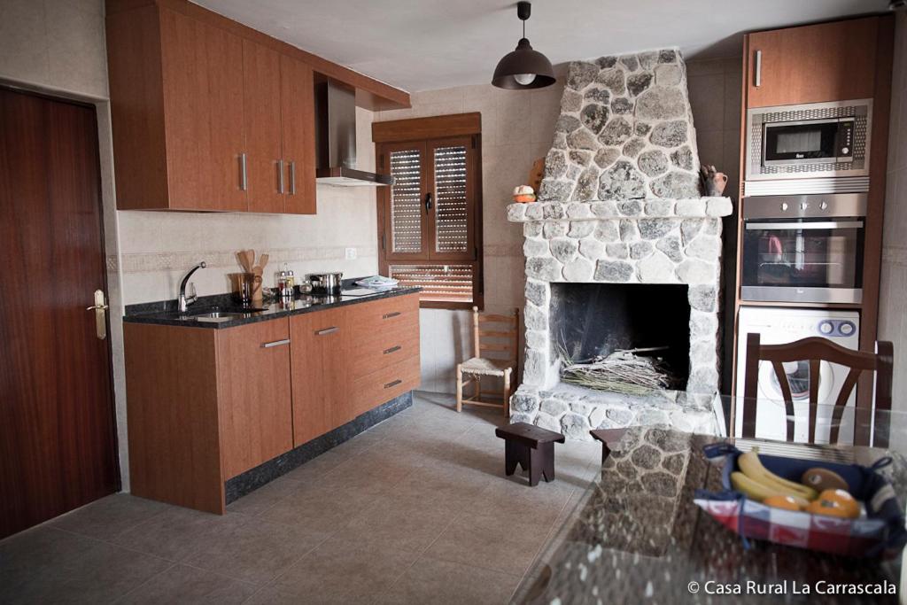 A functional kitchen is equipped with wooden cabinetry and a stone fireplace, enhancing the warm atmosphere. A dining table is visible, alongside a modern oven and a refrigerator, providing essential amenities for meal preparation.