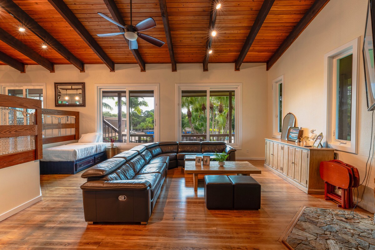 ห้องนั่งเล่นของบ้านสระว่ายน้ำมีที่นั่งหนังหรูหราและมุมเตียงแฝดที่มีเสน่ห์ทั้งหมดนี้อยู่ภายใต้แสงอันอบอุ่นของคานไม้สไตล์ชนบท