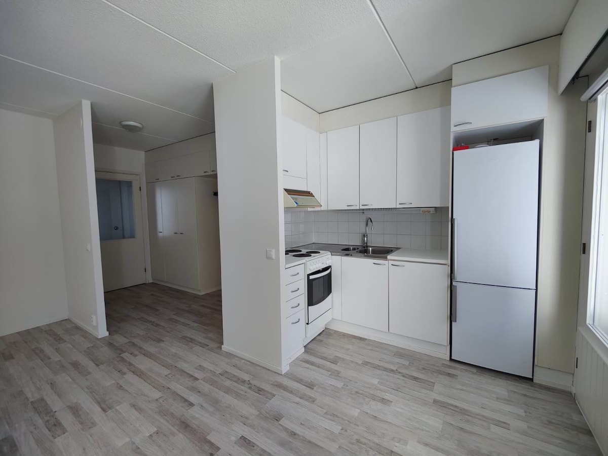 A bright kitchen area features white cabinetry and sleek countertops, equipped with a stove and refrigerator. The open layout creates a connection to the living space, featuring light-colored flooring that enhances the overall spacious feel.