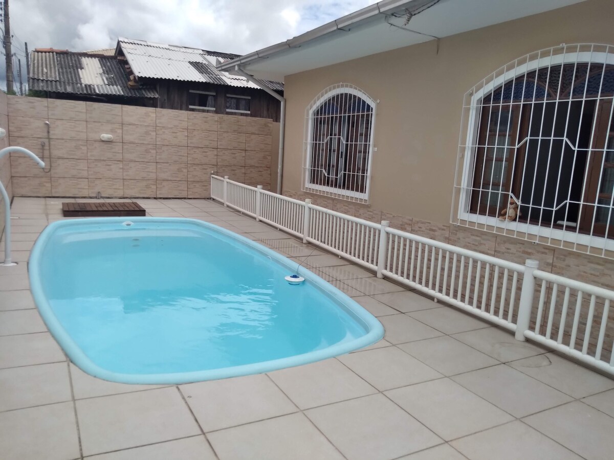 A private pool is situated in a tiled outdoor area, featuring a light blue color. Surrounding the pool, white safety railings provide a secure environment. Large windows and a fence offer visibility while maintaining privacy.