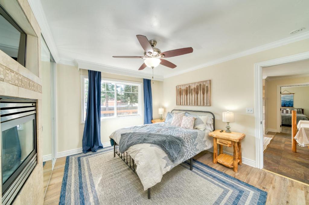 A serene bedroom features a spacious bed with a textured throw blanket. Two bedside lamps illuminate wooden side tables. Natural light filters through a large window covered with blue curtains, while a ceiling fan adds comfort. A gas fireplace adds warmth to the inviting space.