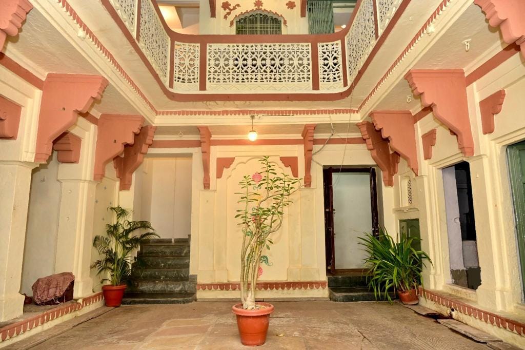 An open courtyard showcases traditional architecture with intricately designed pillars and decorative motifs. Potted plants add greenery, while the arrangement of staircases leads to upper levels. Soft lighting enhances the serene ambiance, inviting guests to explore the interconnected spaces of the home.