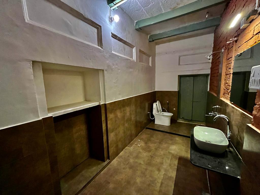 A spacious bathroom features modern fixtures, including a white toilet and a sink set atop a black countertop. The walls are a mix of light and dark tiles, with ample natural light provided by a window, enhancing the room's openness and functionality.