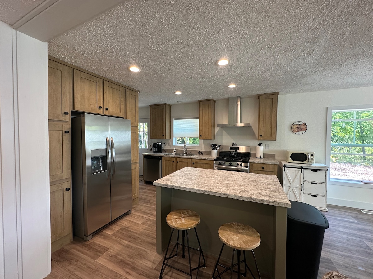 A spacious kitchen showcases modern appliances and ample cabinetry, highlighted by natural lighting from large windows. A central island with seating for two provides a casual dining option. The open layout allows for an inviting and functional cooking environment.