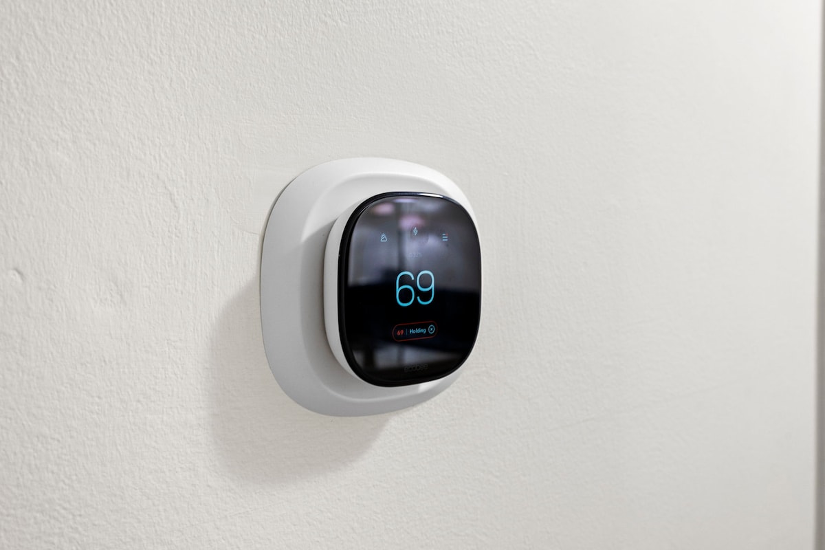 A modern smart thermostat is mounted on a light-colored wall, displaying a digital temperature reading of 69 degrees. The sleek design is minimalistic, enhancing the contemporary feel of the living space.