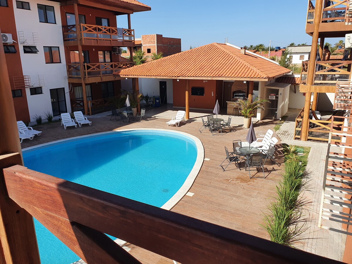The image showcases a well-maintained outdoor area featuring a large turquoise swimming pool surrounded by a wooden deck. Several lounge chairs are positioned near the pool, while a shaded seating area is visible, complete with tables and chairs, enhancing the inviting leisure space.