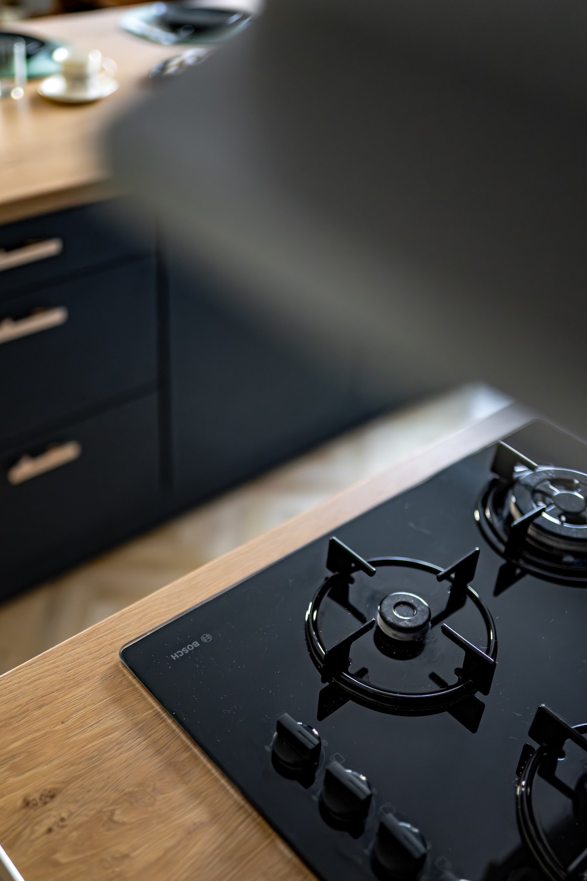 A modern cooktop is featured on a wooden countertop, surrounded by sleek cabinetry. The glossy black surface of the cooktop is complemented by silver knobs, creating a functional and stylish cooking space.