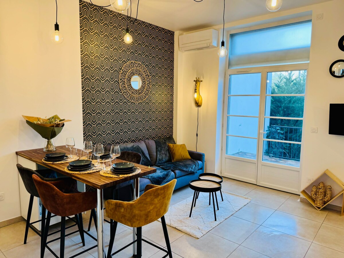 The open living area features a cozy black sofa, complemented by a round table set for dining. A patterned accent wall enhances the space, while large windows allow natural light to fill the room. Unique light fixtures add to the modern decor.