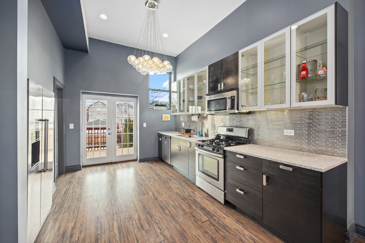 A modern kitchen is featured with stainless steel appliances, including a gas stove and oven. Ample cabinetry offers storage space, complemented by a light granite countertop. A large window allows natural light to brighten the area, while stylish pendant lighting hangs overhead.