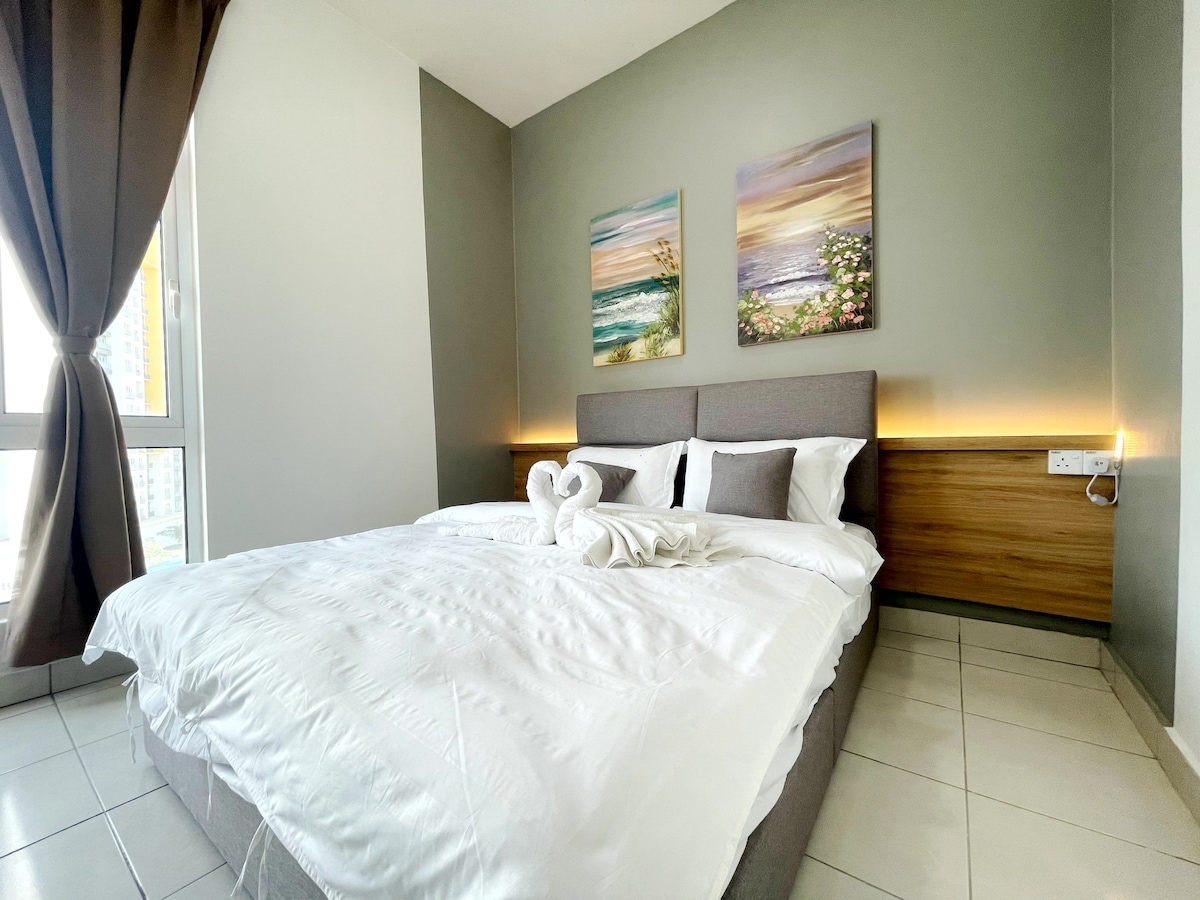 A bright master bedroom features a spacious bed with soft linens and decorative cushions. Two framed paintings adorn the wall, adding a touch of color. Natural light enters through large windows, and subtle lighting enhances the ambiance.