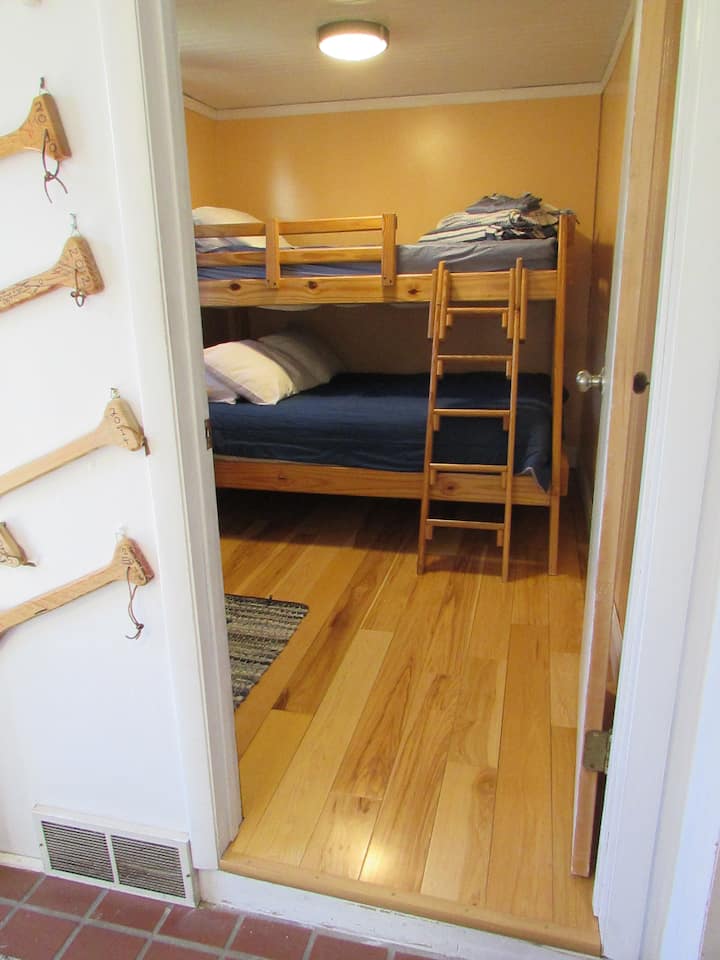 Ľahká broskyňová spálňa s drevenou podlahou, dvojitou posteľou na vrchu a manželskou posteľou v spodnej časti.