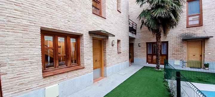 Patio comunitario con césped y palmera junto a la entrada de la casa.