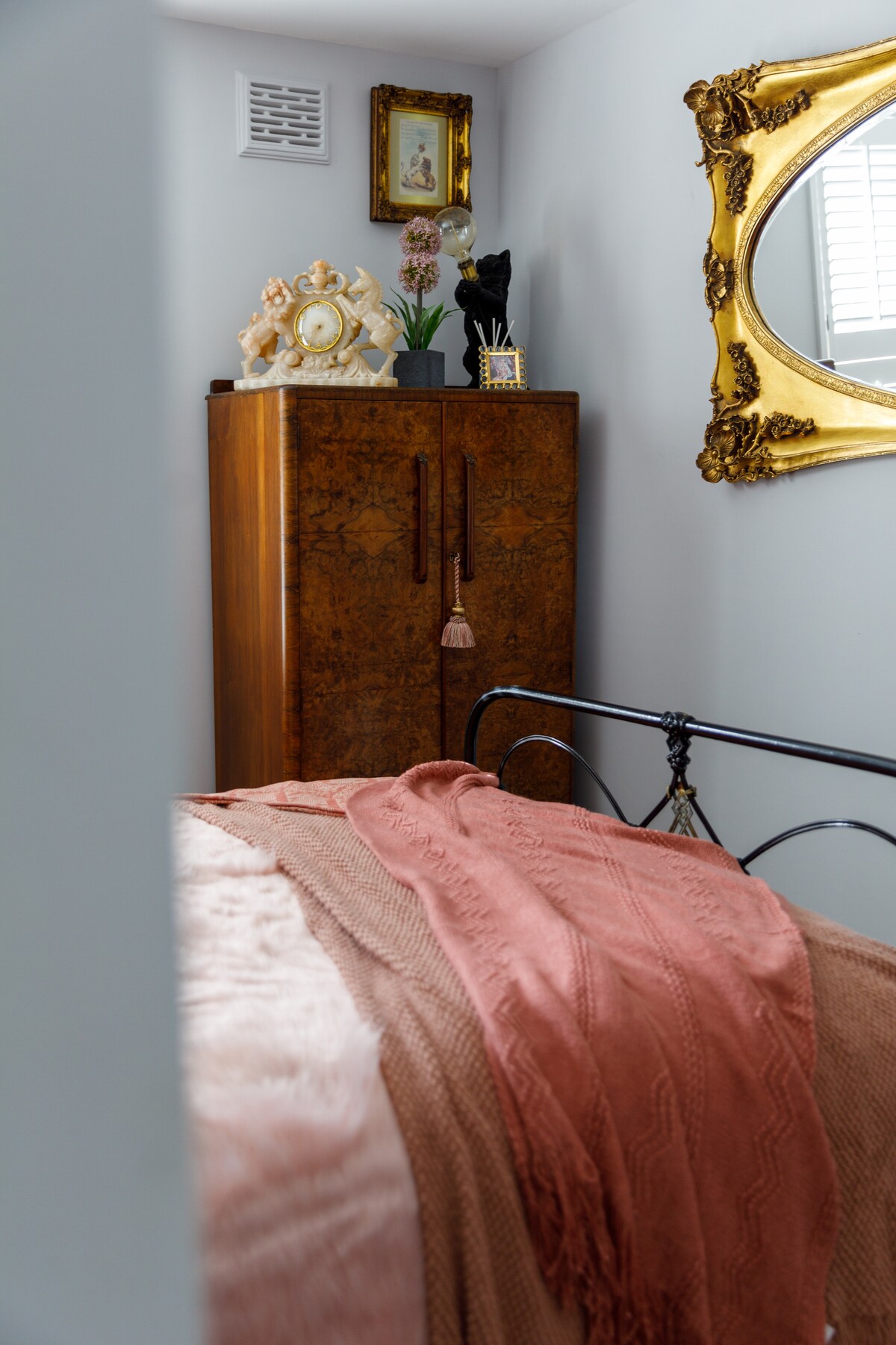 Შესასვლელი ვარდისფერ საძინებელში საწოლით წინა პლანზე და გარდერობი ფონზე, სადაც ნაჩვენებია ლომი და უნიჭო საათი და შავი კატის ნათურა