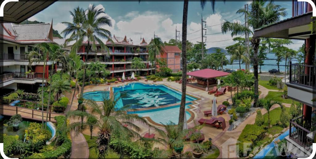 The image showcases a vibrant pool area surrounded by lush greenery and palm trees. Lounge chairs are positioned around the large swimming pool. The layout includes multiple levels of the building, with an ocean view visible in the background, highlighting an inviting outdoor environment.