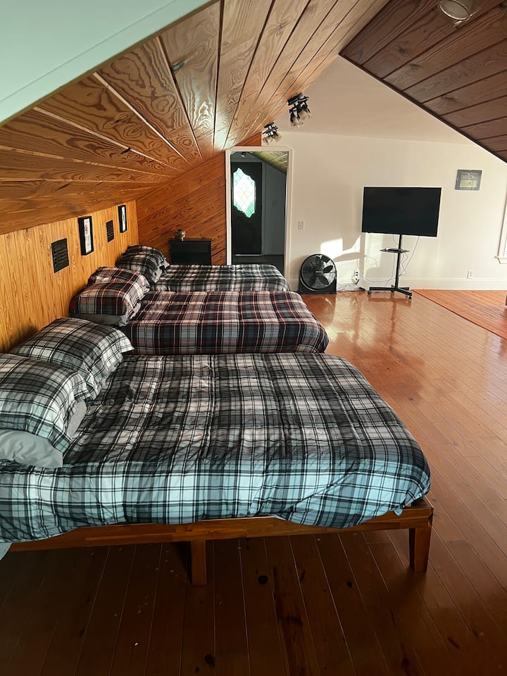 غرفة نوم في الطابق العلوي بثلاثة أسرّة كاملة الحجم وتلفزيون ومنطقة جلوس