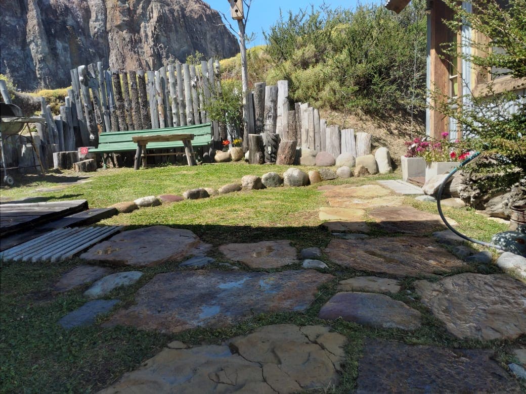 A stone pathway leads through a garden featuring a wooden bench and a rustic fence. Surrounding plants and flowers add natural beauty to the outdoor space, while the mountains serve as a scenic backdrop.