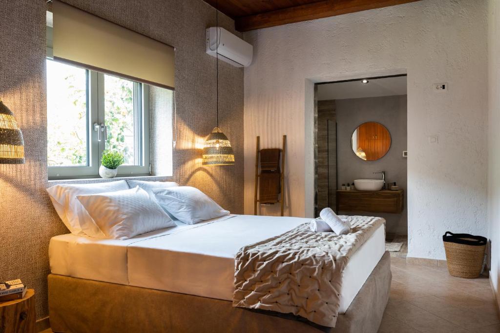 A serene bedroom features a spacious bed with white linens and a textured throw blanket. Natural light filters through a window adorned with a soft shade. Hanging pendant lights add a warm glow, while an open doorway leads to a stylish bathroom with modern fixtures.