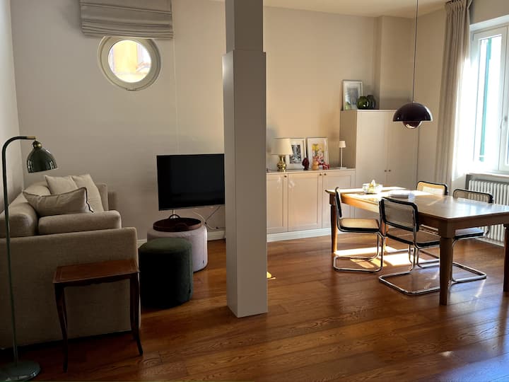 Ხედი შესასვლელიდან მთავარი ოთახისკენ დივნით (საწოლის დივანი ორი ცალკეული საწოლით) და სასადილო სივრცით. 