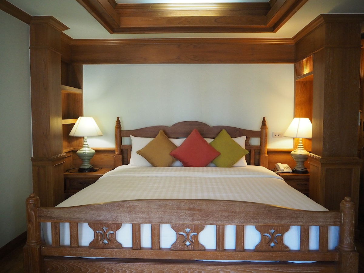 A comfortable sleeping area features a wooden bed with a high headboard. Soft pillows in varied colors are placed against the headboard. Wooden nightstands with lamps are positioned on either side, adding to the cozy ambiance.