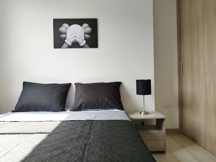 ダブルベッド、モダンなランプ付きのナイトスタンド、スライドドア付きの広々としたクローゼットを備えた客室。自然光がミニマリストスタイルを際立たせ、装飾的な絵が空間にエレガントで居心地の良い雰囲気を与えています。

