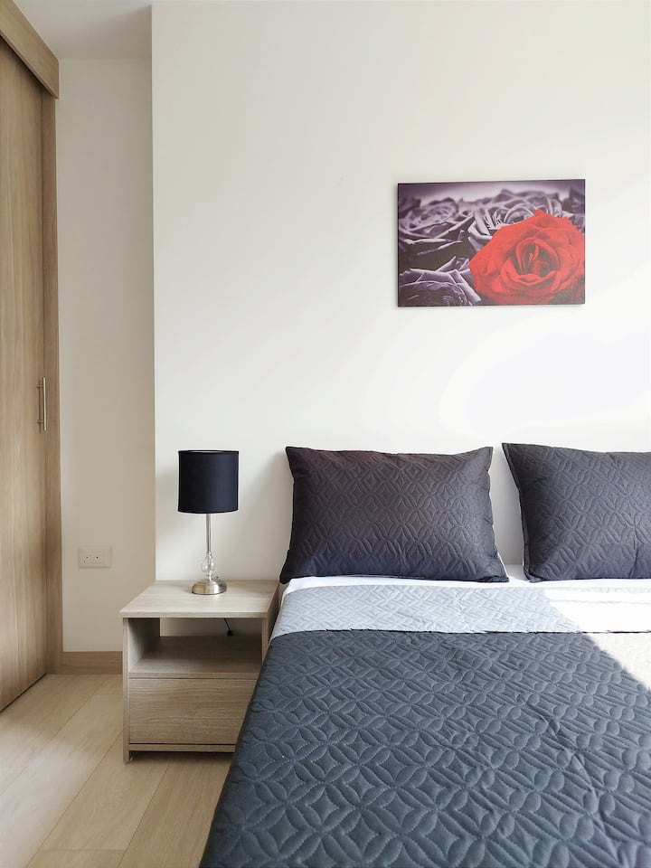 ダブルベッドとエレガントなグレーのベッドリネンを備えた居心地の良い客室。モダンなランプが置かれたベッドサイドテーブル、木製クローゼット、そして空間に暖かく洗練された雰囲気を添える装飾画が含まれています。

