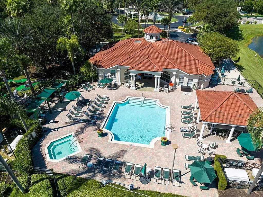 An aerial view of the resort's main pool area showcases a large swimming pool with a surrounding patio. Sun loungers are arranged neatly, while additional shaded seating areas are provided. Lush palm trees and well-manicured landscaping enhance the tranquil ambiance.