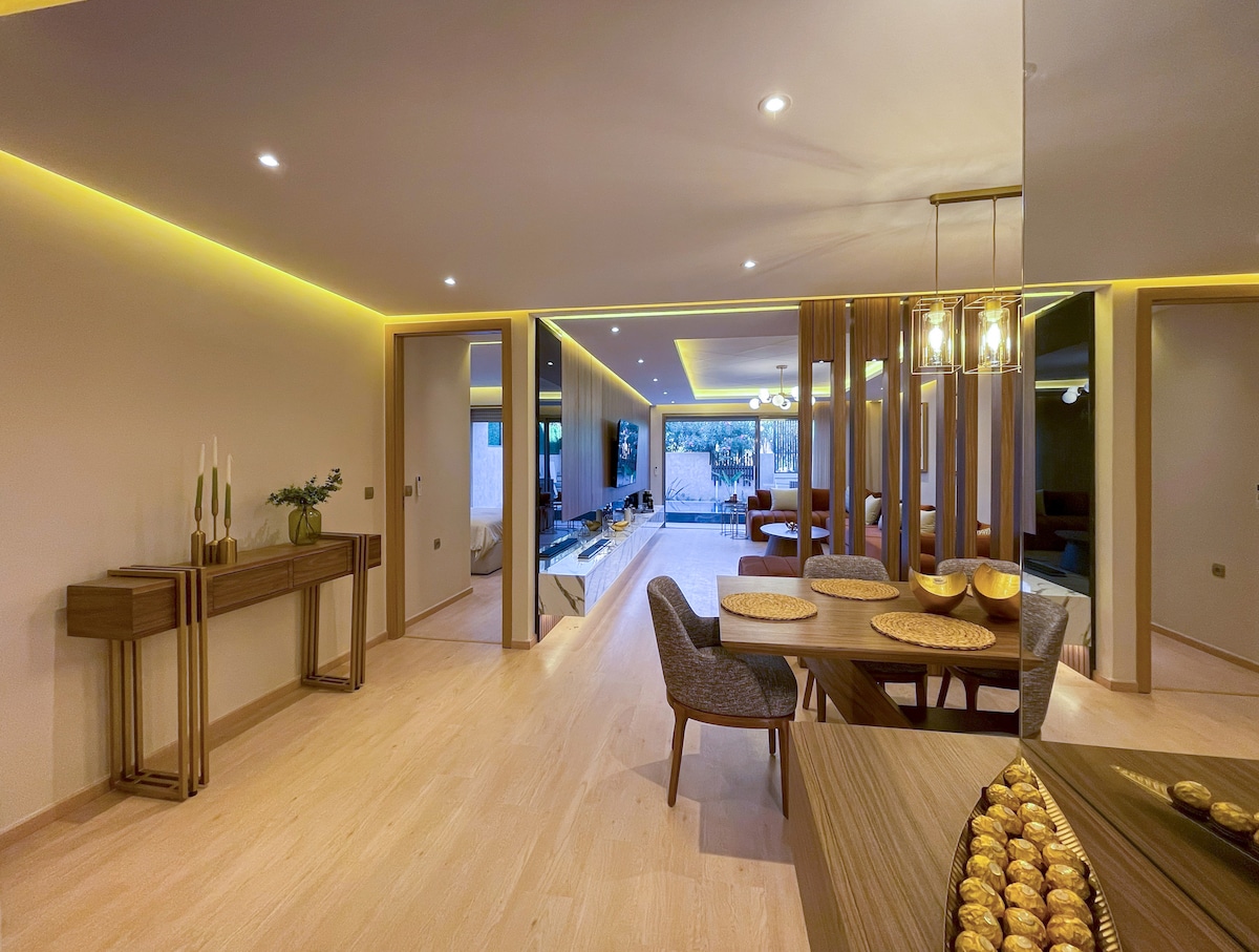 A modern dining area is showcased, featuring a wooden table set for six. Soft ambient lighting enchances the spacious atmosphere. Elegant seating arrangements are complemented by decorative bowls on the table. Large sliding glass doors lead to an outdoor space, allowing for ample natural light.