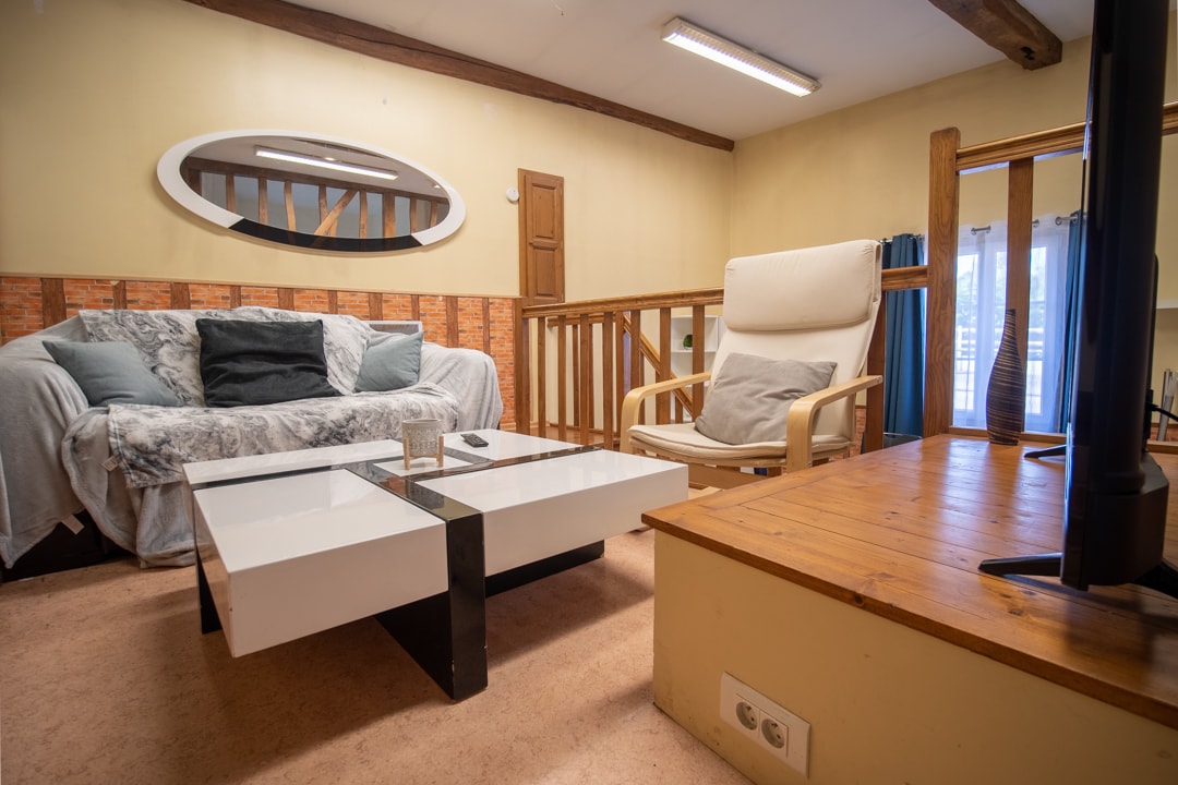 A spacious living area is showcased with a light-colored sofa draped in a soft blanket and a modern coffee table. Natural light filters in through the balcony doors, which open to a view of the outdoors, accentuating the warm, neutral tones of the walls.