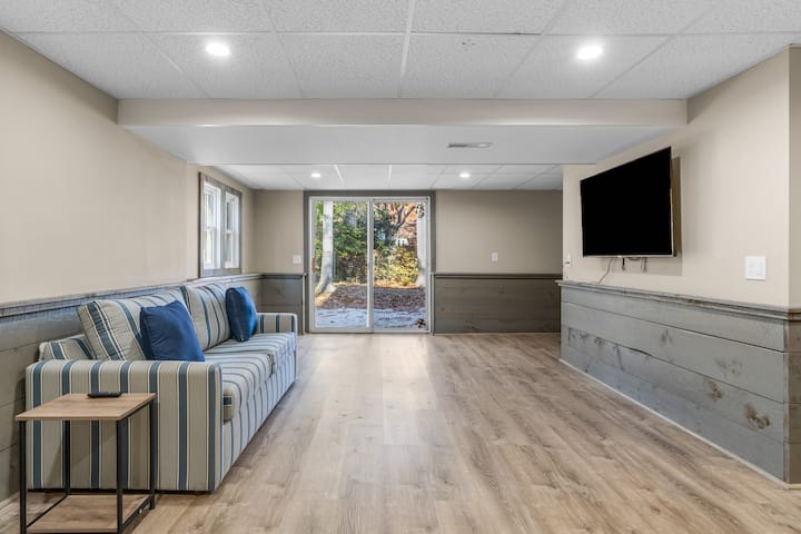 מרחב מחיה נוסף במרתף עם טלוויזיה חכמה עם מסך שטוח גדול, דלתות הזזה המובילות לחצר האחורית וספה נפתחת בגודל קווין סייז!
