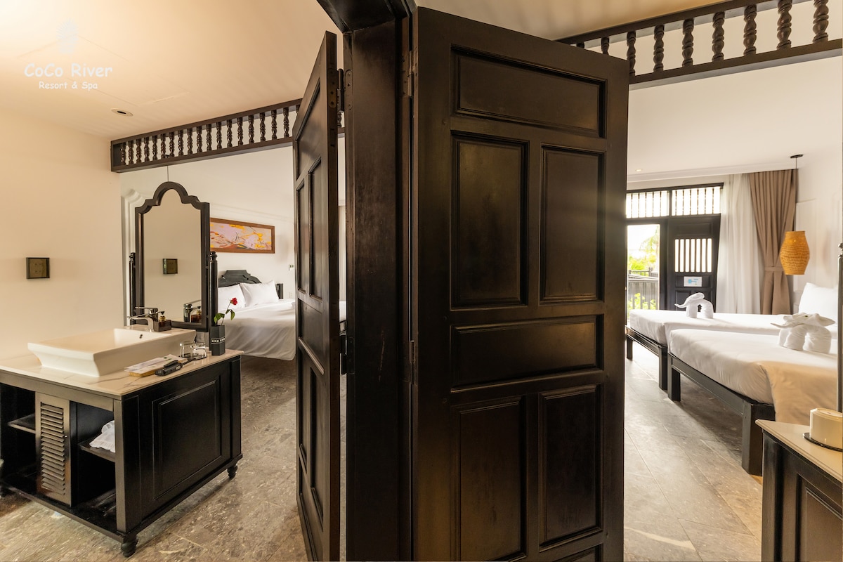 A view showcasing an elegant room divider that separates two sleeping areas. The dark wooden doors lead to a spacious layout with natural light filtering through windows. A stylish dresser is visible on the left, complementing the modern decor.